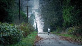 man-walking-down-hill-road-distance-wide-shot-wooded-hillside-cars-passing-nearby-81464531